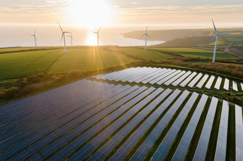 Rows of solar panels and wind turbines on a coastal field at sunset