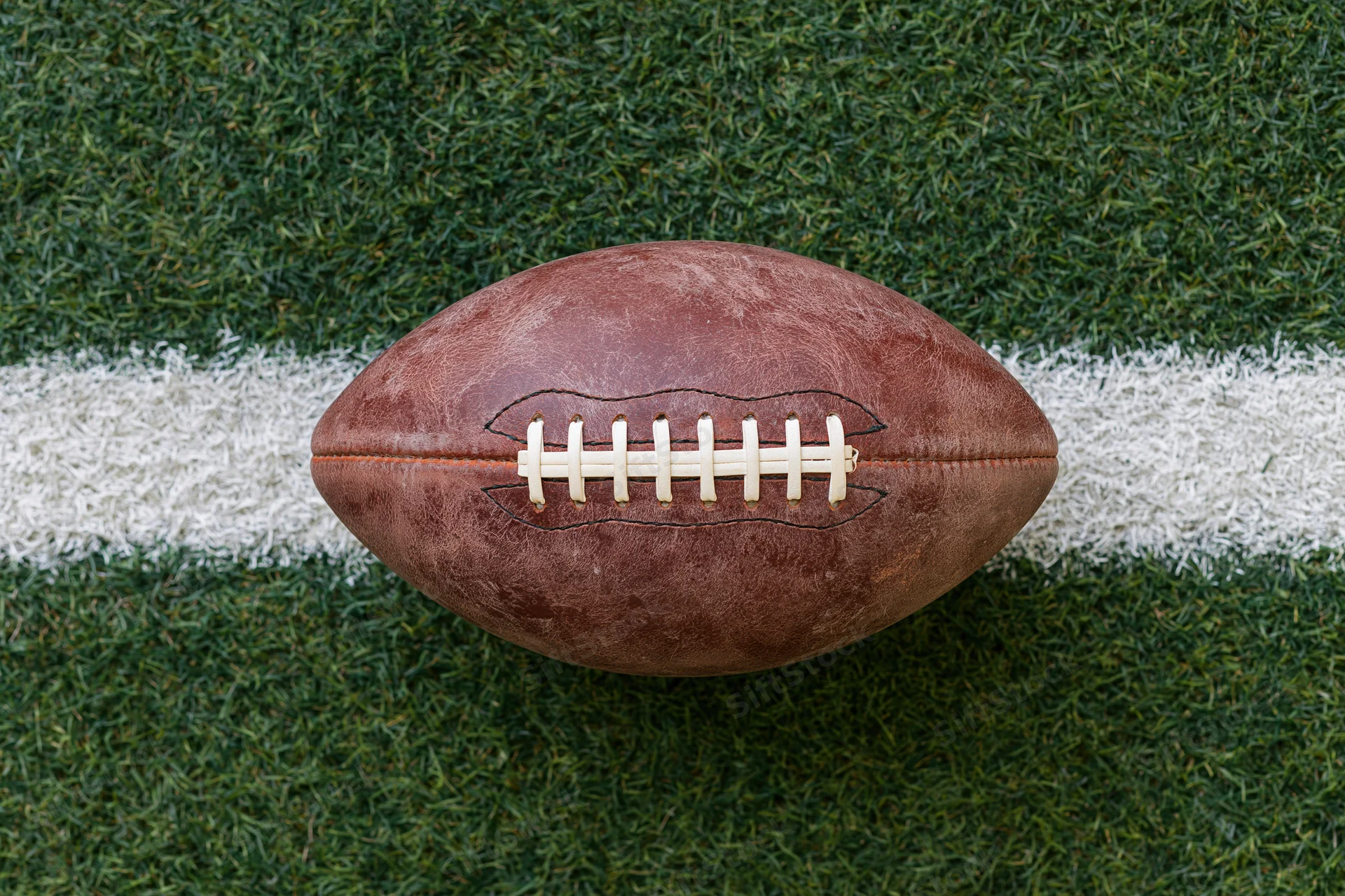 American football resting on a white yard line of a green turf field