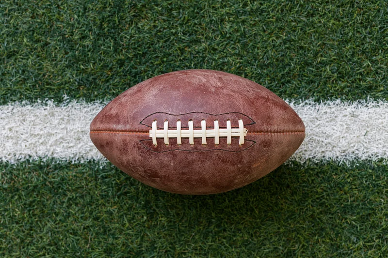 American football resting on a white yard line of a green turf field