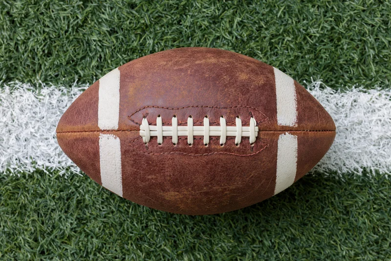 American football resting on painted white yard line on green turf field