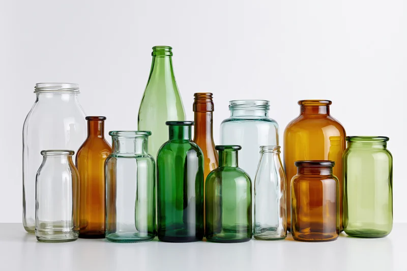 Assorted empty glass bottles and jars of varying heights arranged on a white surface