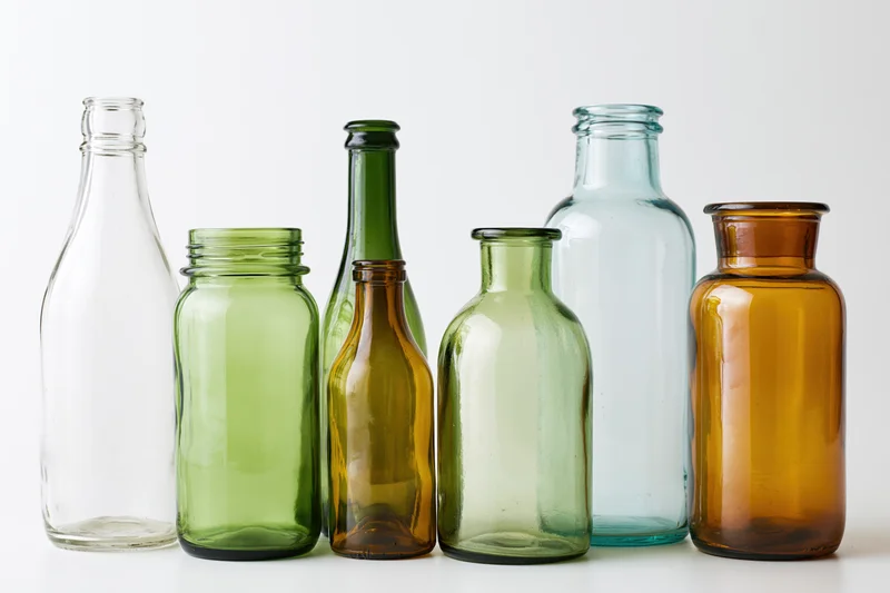 Assorted empty glass bottles and jars arranged in a row on a white surface