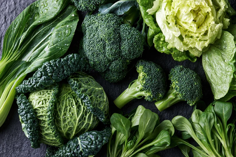 Assorted green vegetables arranged on dark surface with water droplets