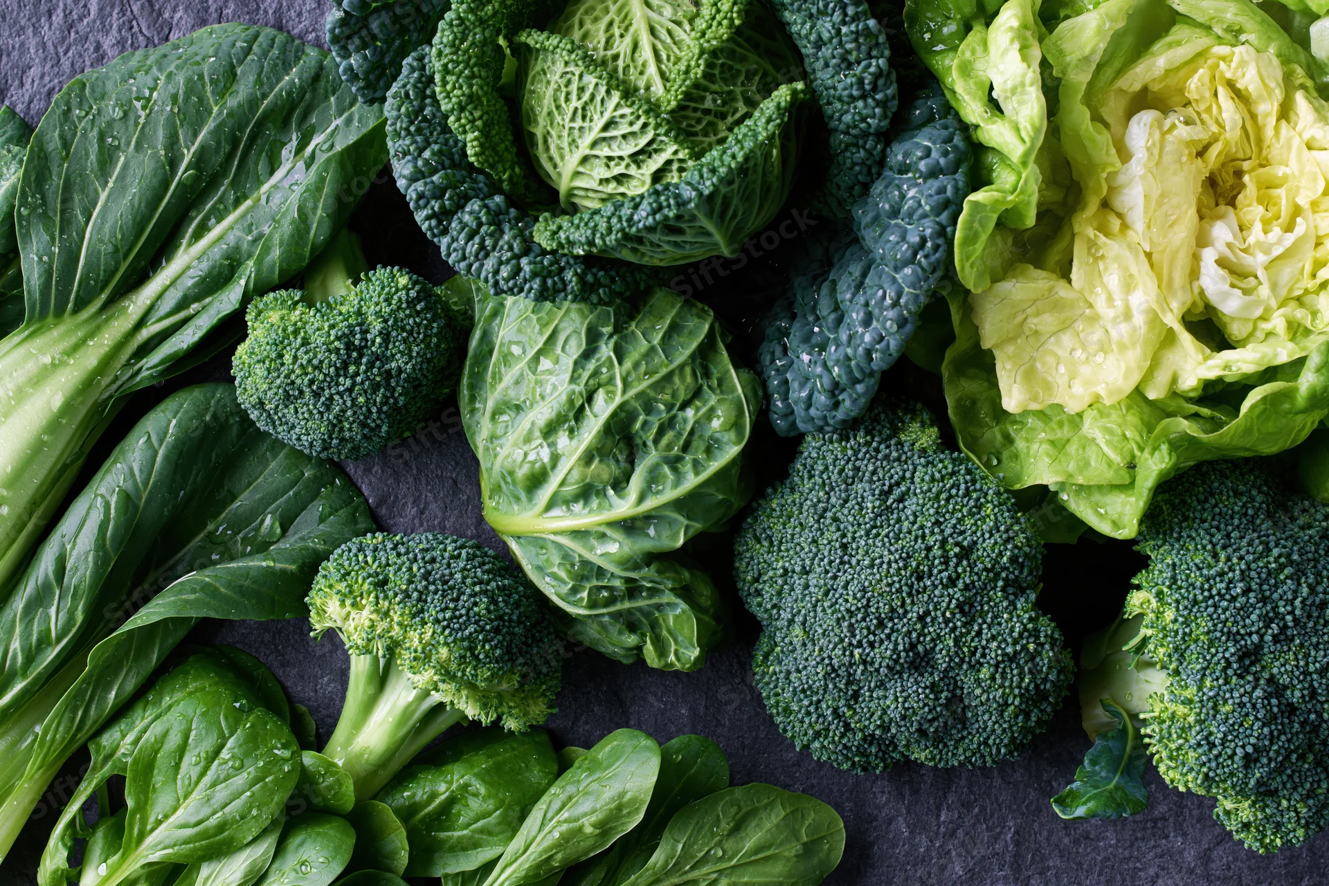 Assorted green vegetables arranged on dark slate surface