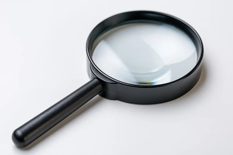 Black magnifying glass with glossy lens resting diagonally on white surface