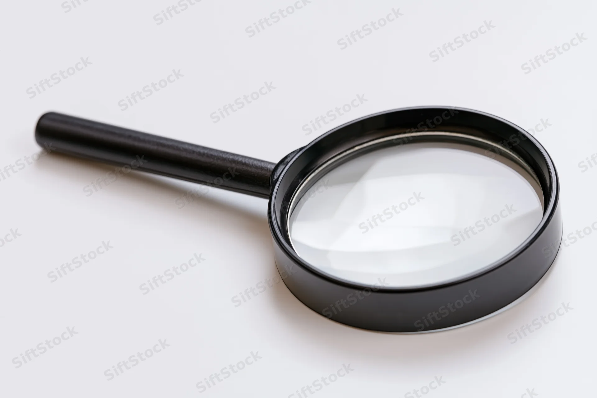 Black magnifying glass with glossy lens resting diagonally on white surface