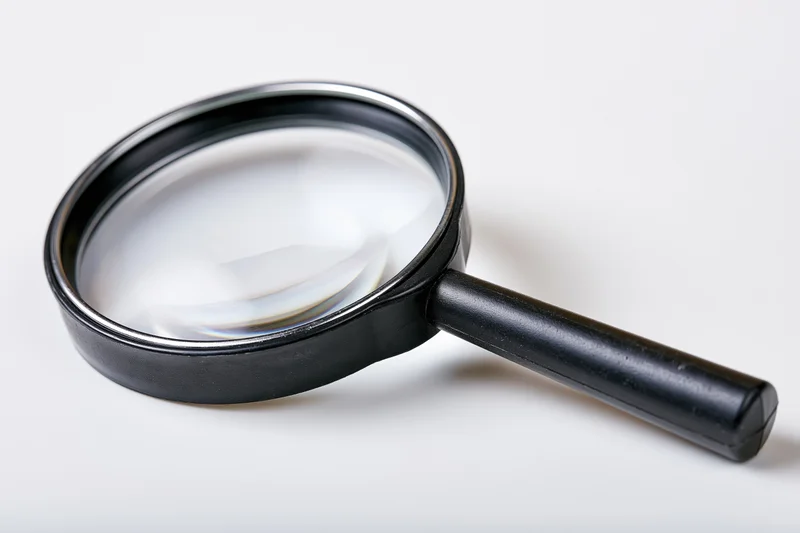 Black magnifying glass with glossy lens resting diagonally on white surface
