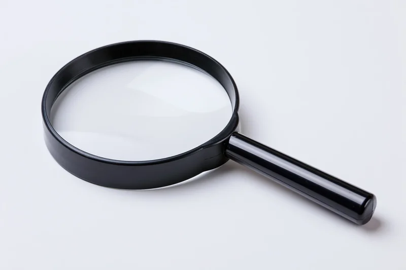 Black magnifying glass with glossy plastic handle resting on white surface