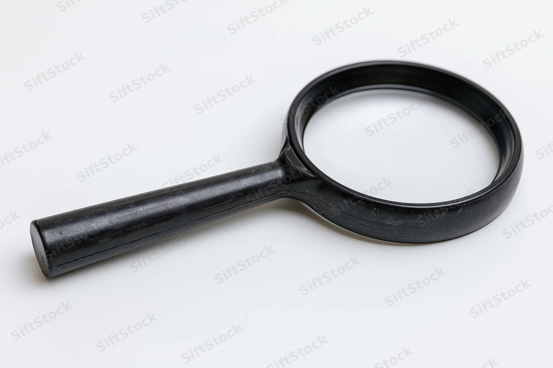 Black plastic magnifying glass with cylindrical handle lying on white surface