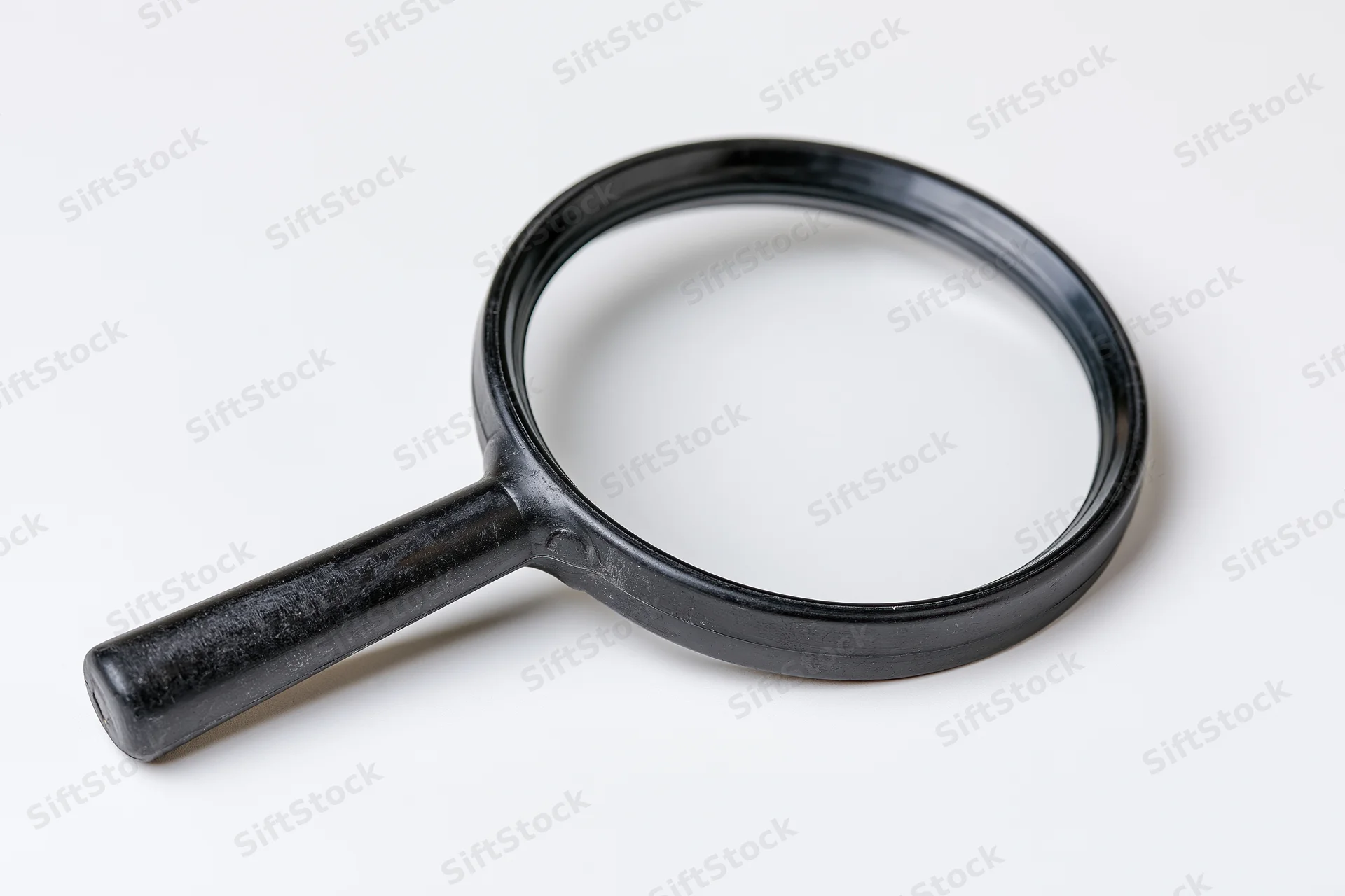 Black plastic magnifying glass with cylindrical handle resting on white surface