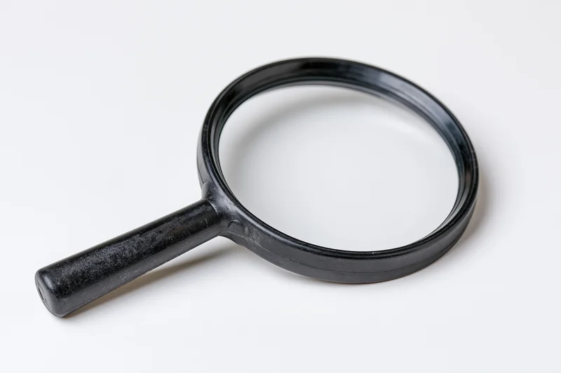 Black plastic magnifying glass with cylindrical handle resting on white surface