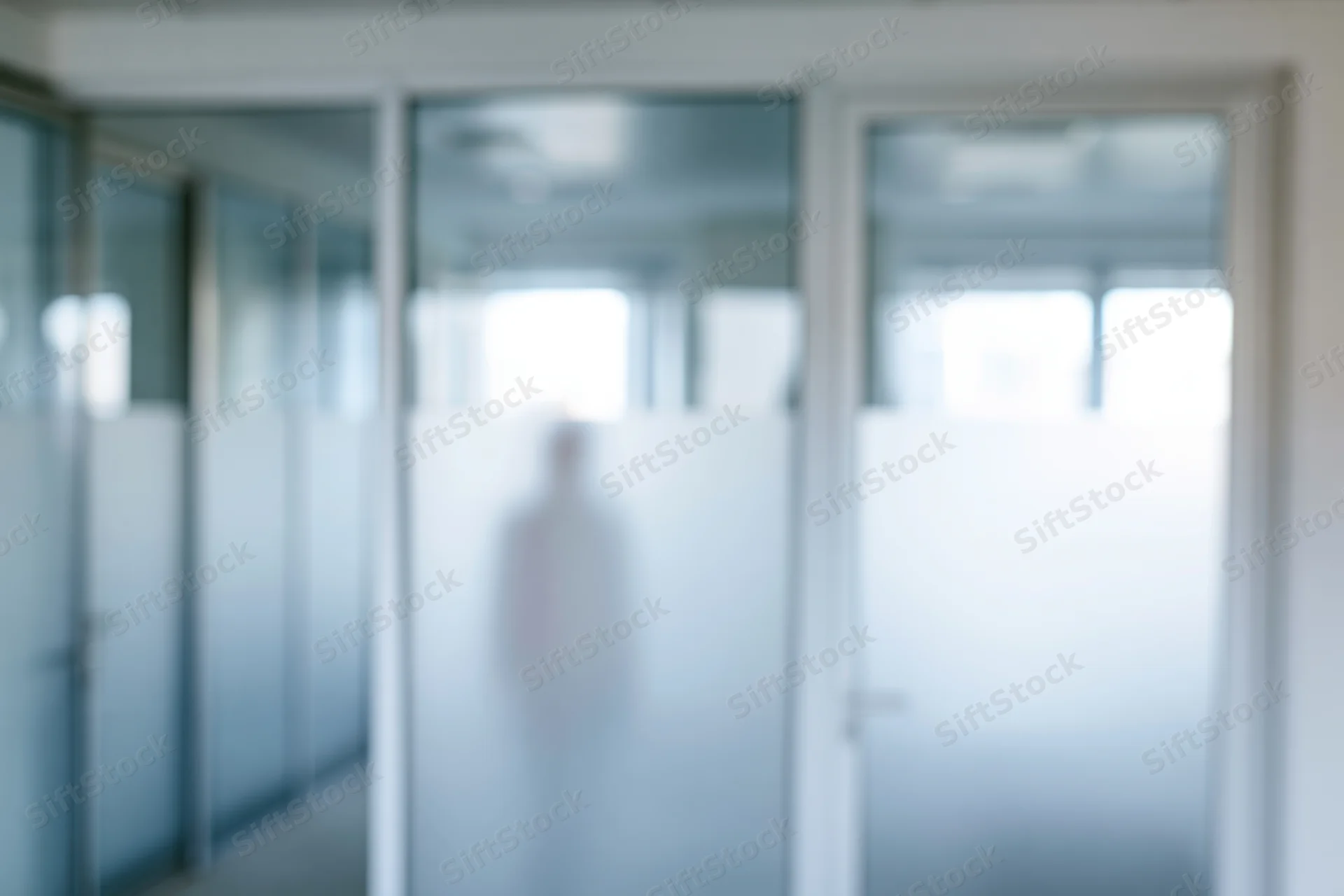 Blurred view through frosted glass office partition showing a silhouette in a hallway