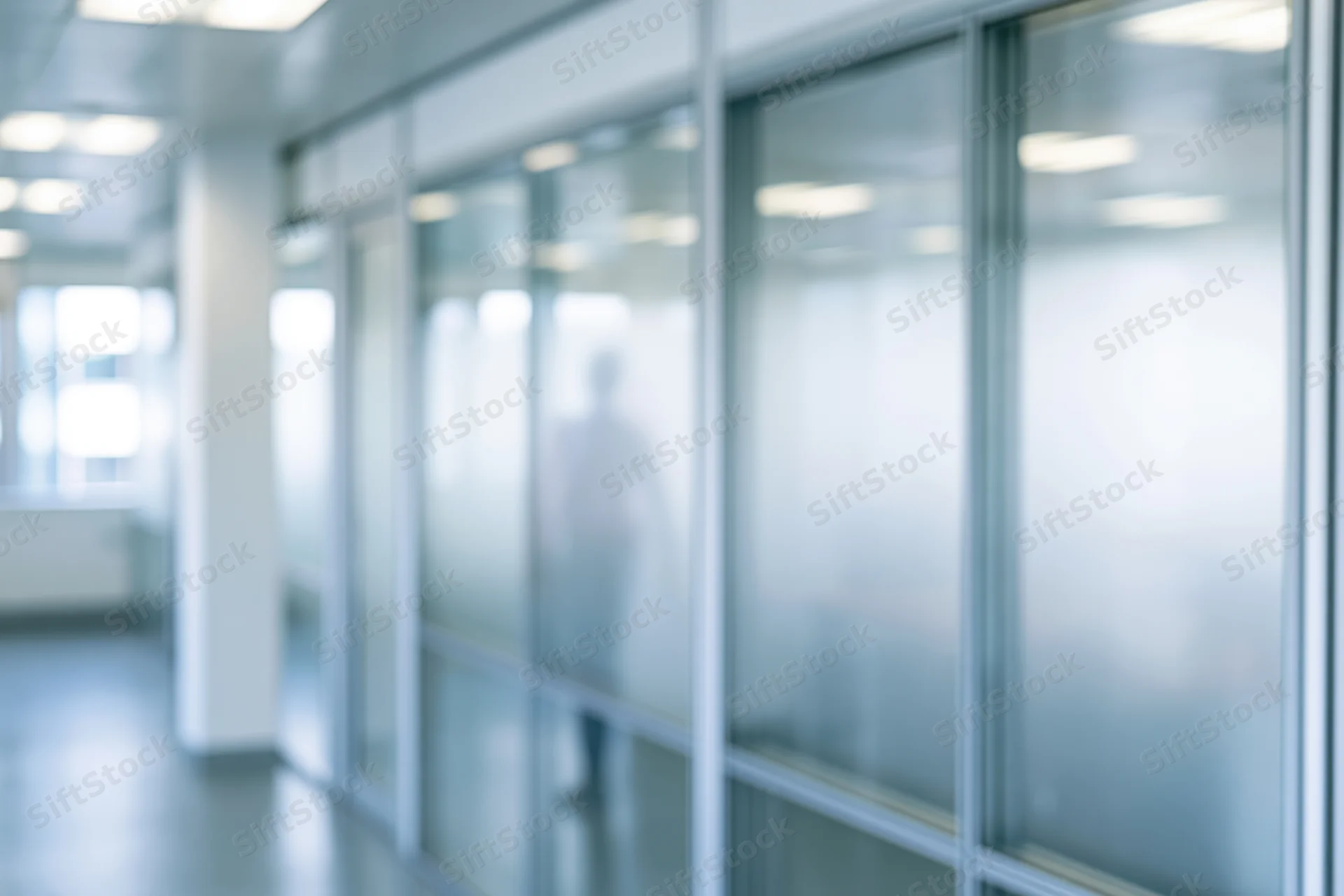 Blurred view through frosted glass office partition showing a walking silhouette in a modern corridor