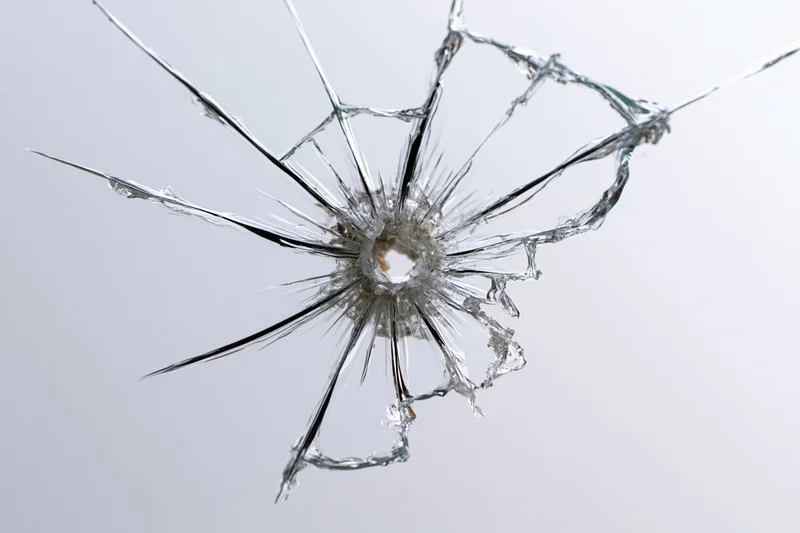 Broken glass pane with central impact point radiating cracks against white background