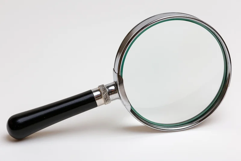 Classic magnifying glass with black handle and silver chrome frame on white background