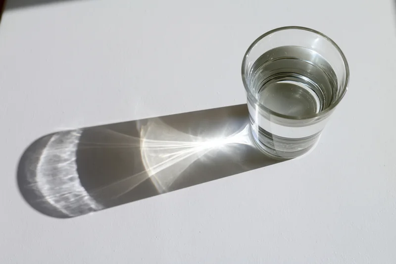 Clear glass filled with water casting a refracted light shadow on a white surface