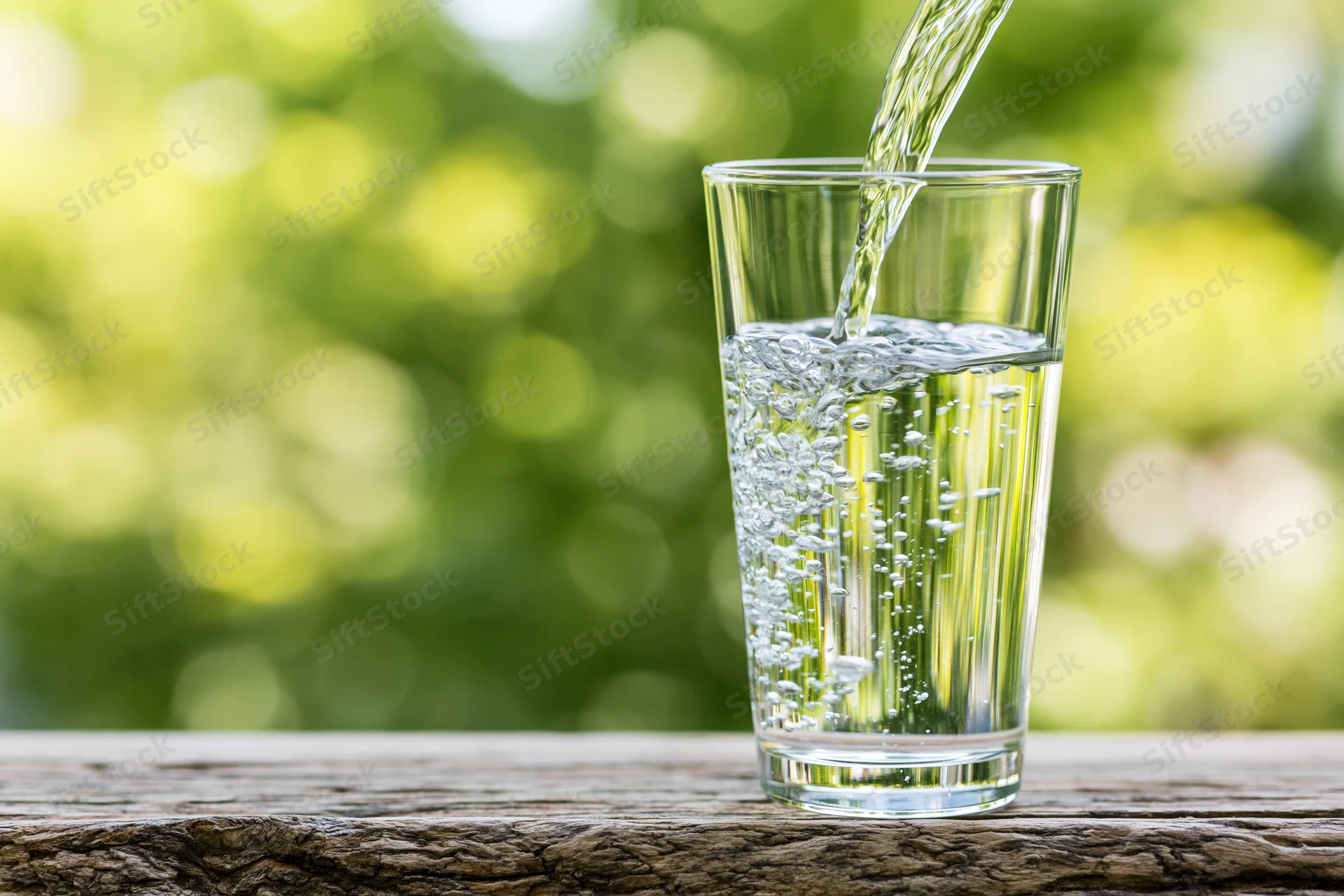 Clear water being poured into a tall glass on a wooden table outdoors