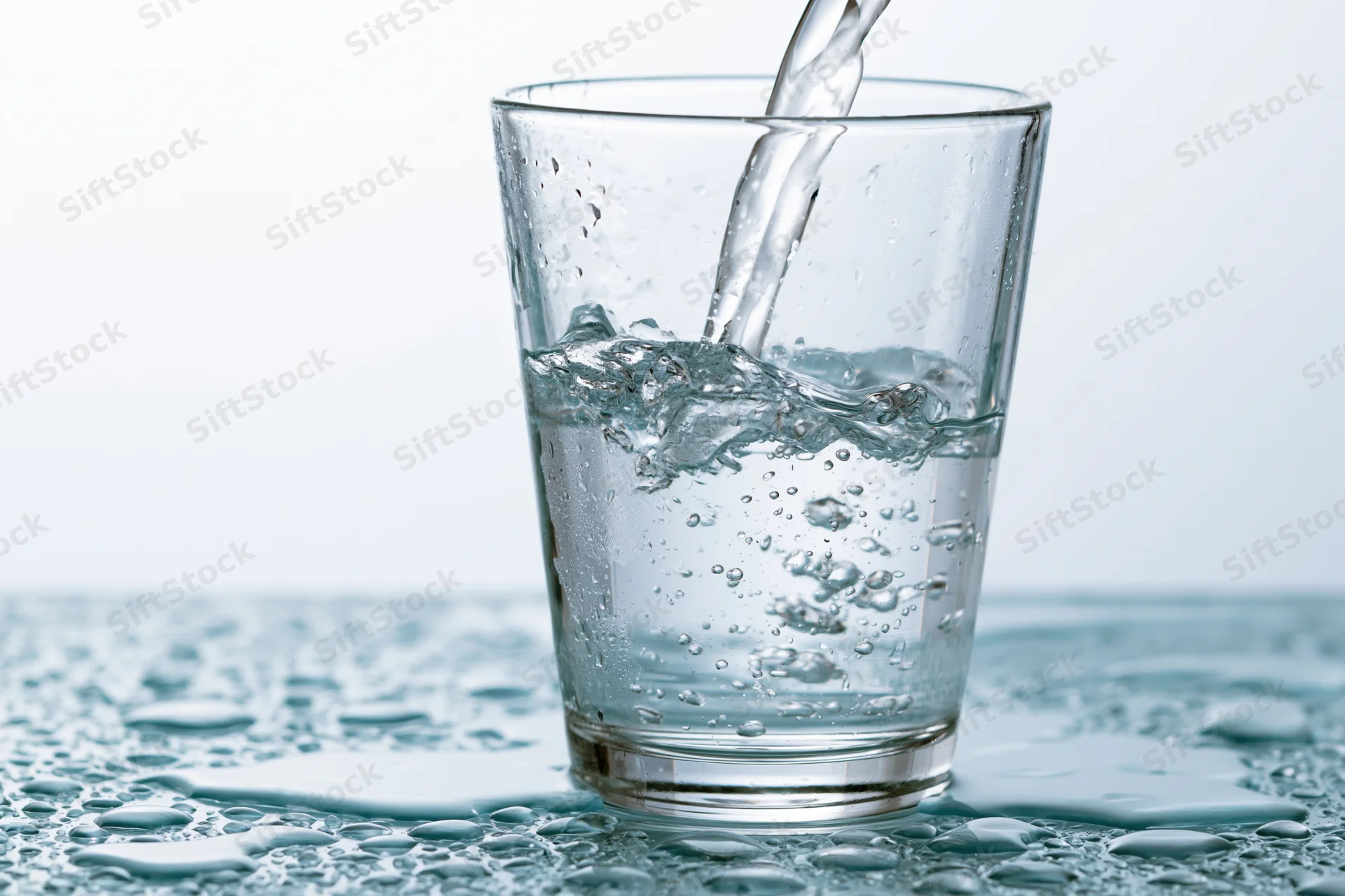 Clear water being poured into a tall drinking glass on a wet surface