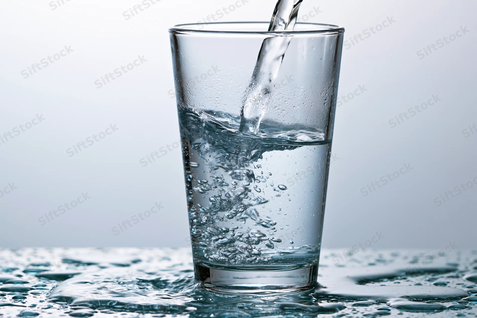 Clear water being poured into a tall drinking glass on a wet surface