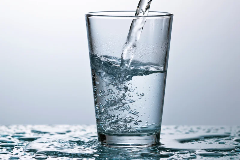 Clear water being poured into a tall drinking glass on a wet surface