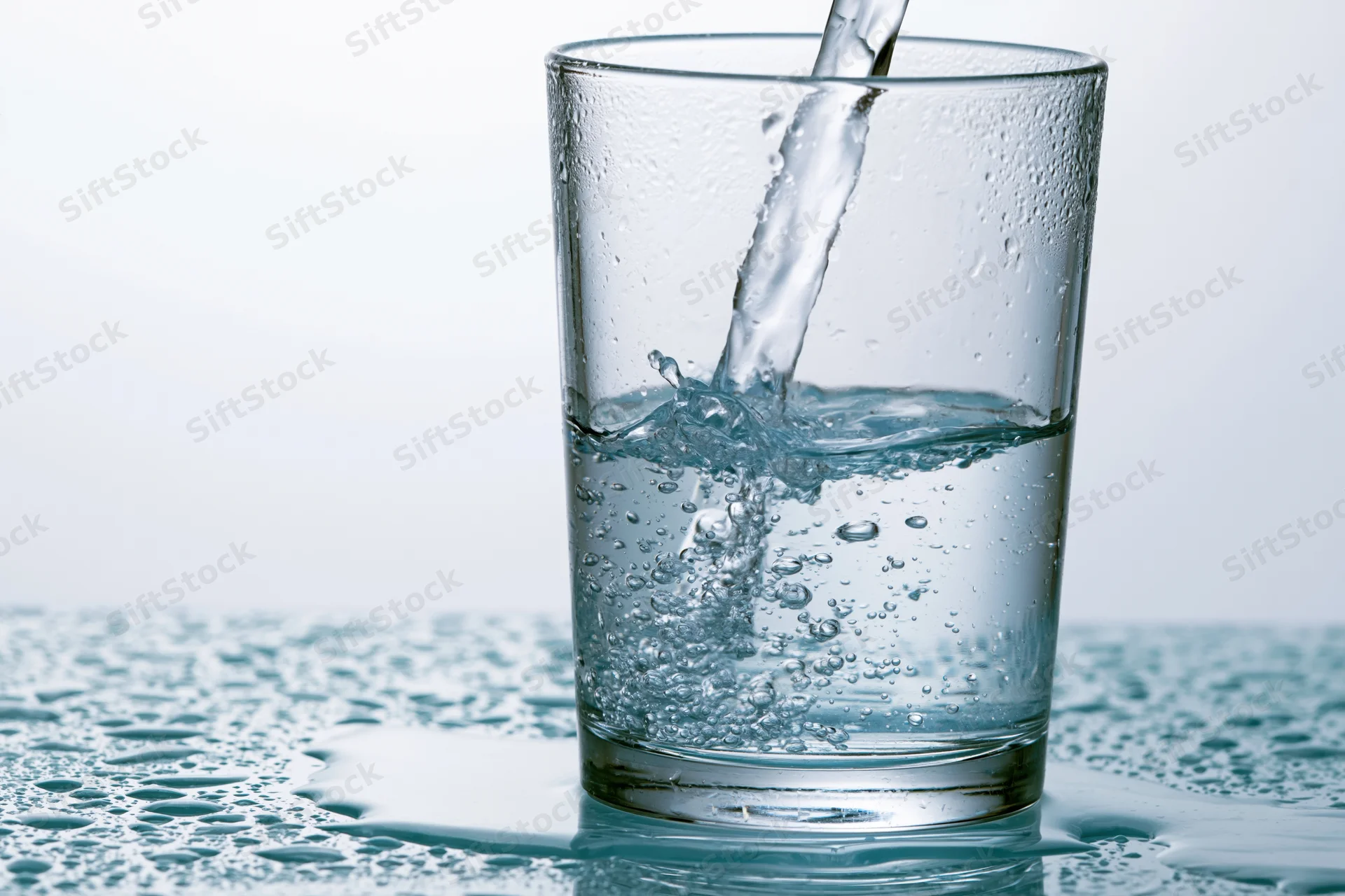Clear water being poured into a tall drinking glass on a wet surface