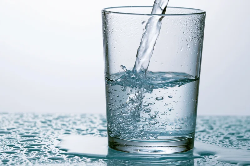 Clear water being poured into a tall drinking glass on a wet surface