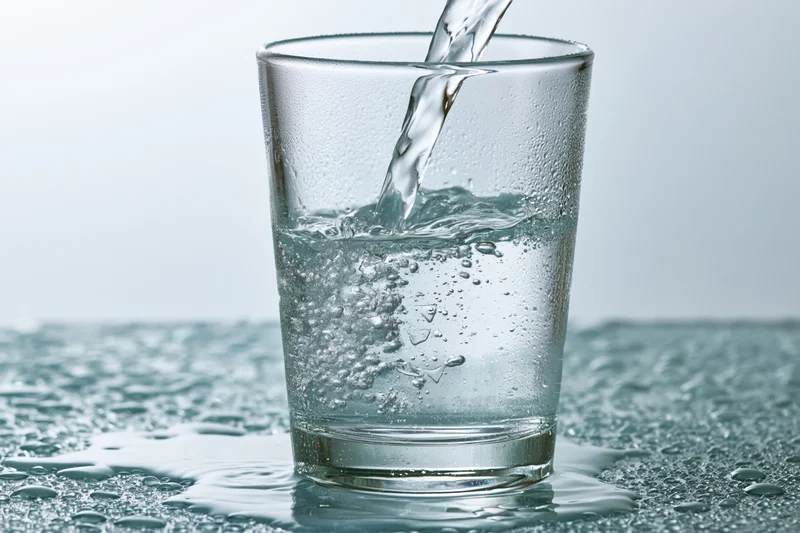 Clear water being poured into a tall drinking glass on a wet surface