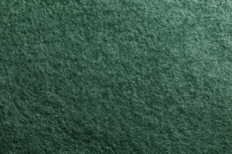 Close-up flat lay of dark forest green felt or suede fabric surface
