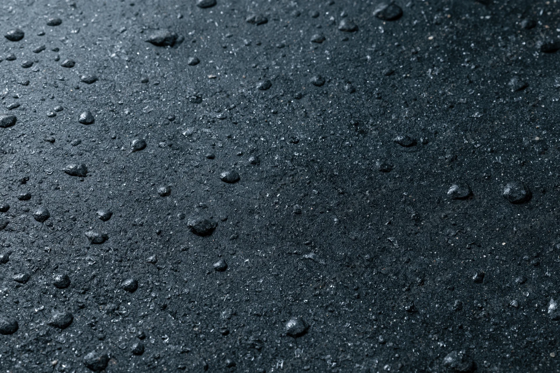 Close-up of wet dark concrete surface with water droplets scattered across it