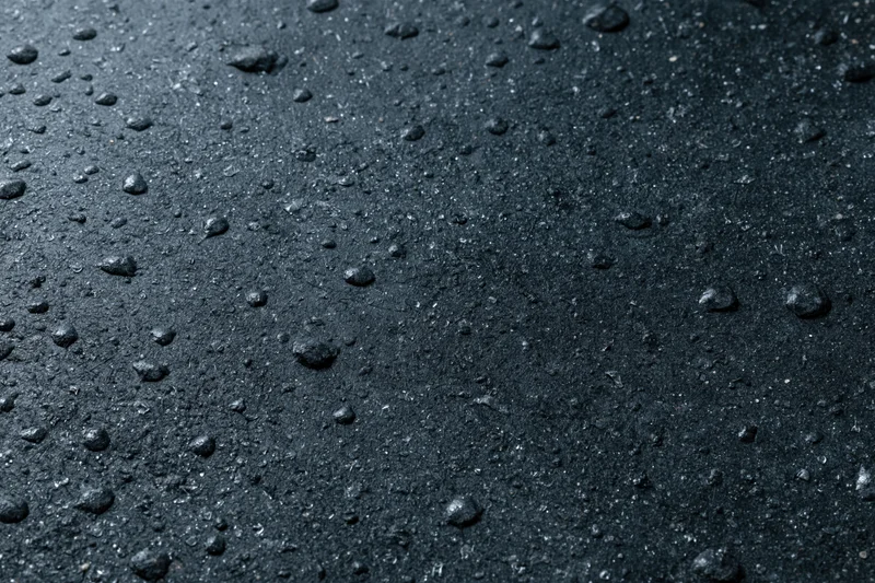 Close-up of wet dark concrete surface with water droplets scattered across it