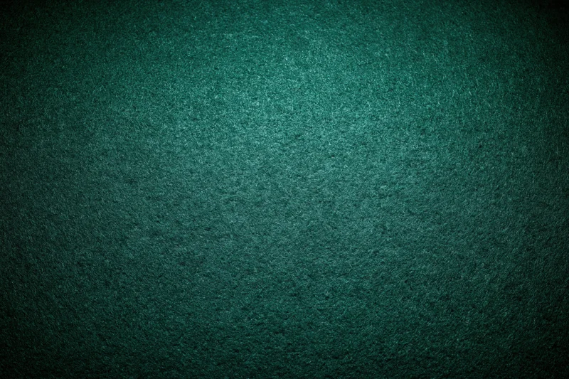 Close-up flat lay of green felt poker table surface with textured grain and dim lighting