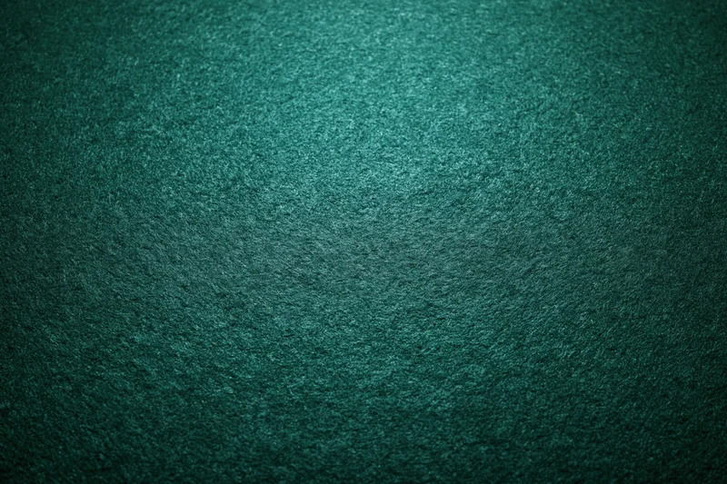 Close-up flat lay of green felt poker table surface with textured weave and subtle lighting gradient