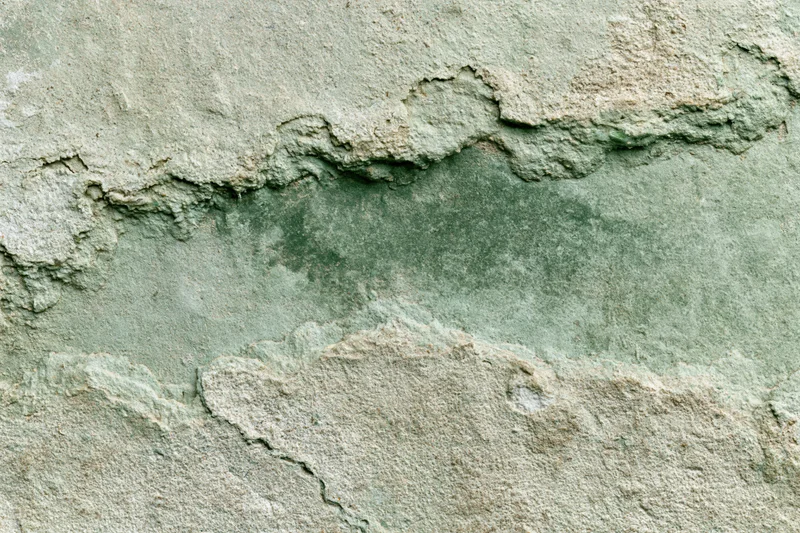 Close-up of aged concrete wall surface with cracked and peeling texture showing weathering and discoloration