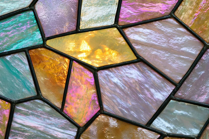 Close-up of an iridescent stained glass mosaic panel with geometric shapes and vibrant colors arranged in a flat lay