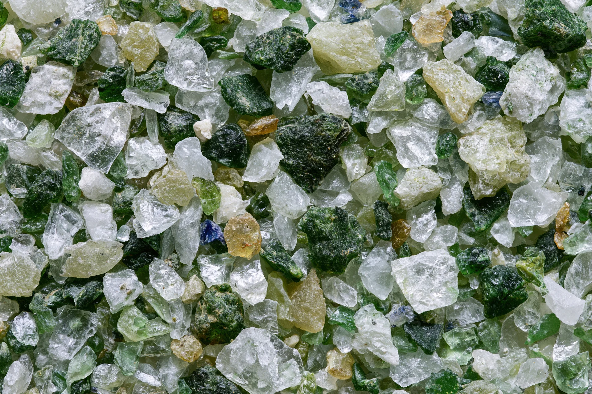Crushed recycled glass cullet spread flat in a dense layer showing varied green, clear, and colored fragments