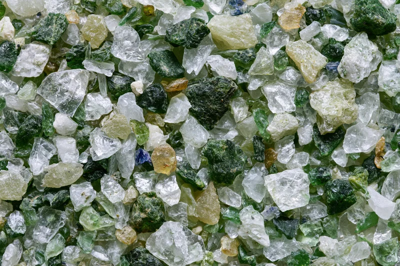 Crushed recycled glass cullet spread flat in a dense layer showing varied green, clear, and colored fragments