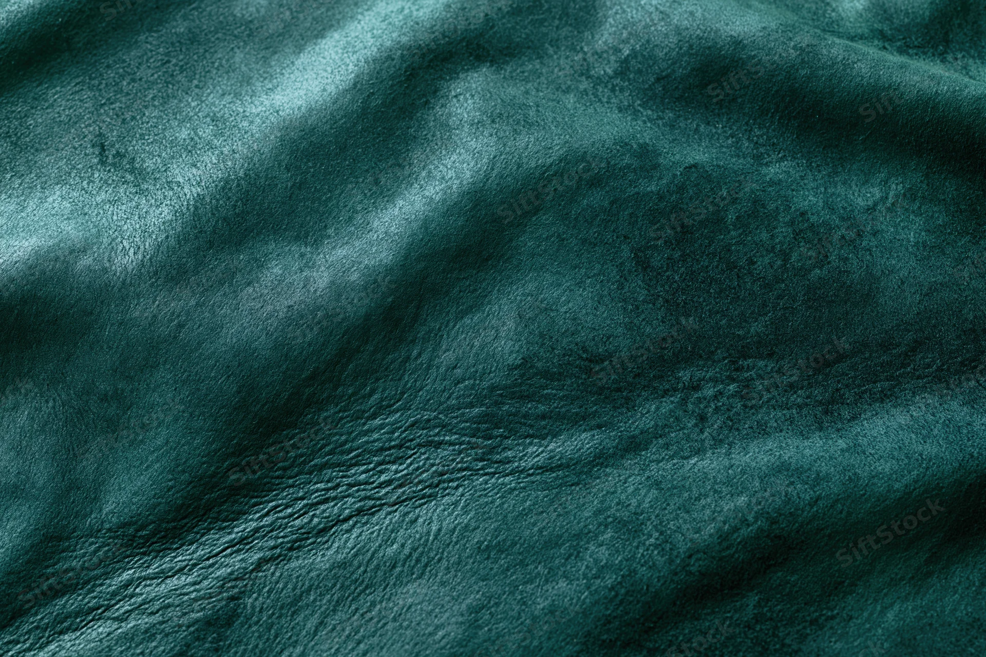 Close-up flat lay of dark forest green leather or suede material with visible texture and wrinkles