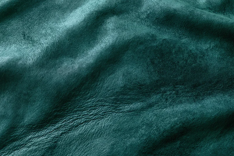 Close-up flat lay of dark forest green leather or suede material with visible texture and wrinkles