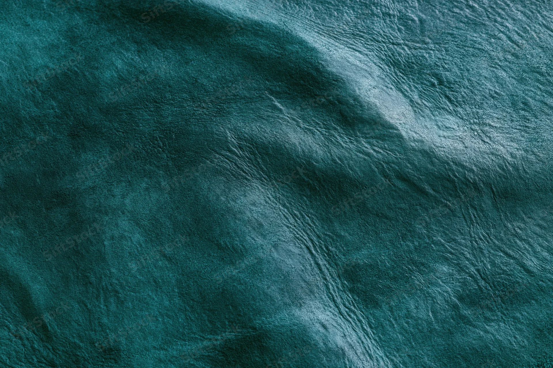 Close-up flat lay of dark forest green leather or suede material with natural texture and folds