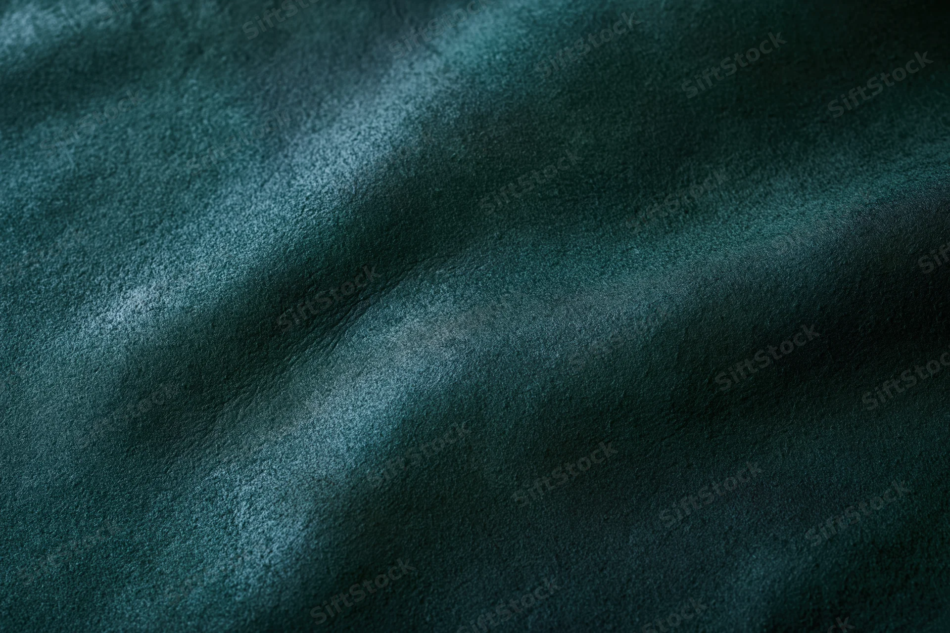 Close-up flat lay of dark forest green leather or suede material showing texture and grain
