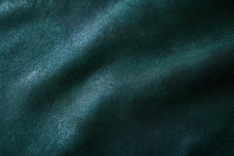 Close-up flat lay of dark forest green leather or suede material showing texture and grain
