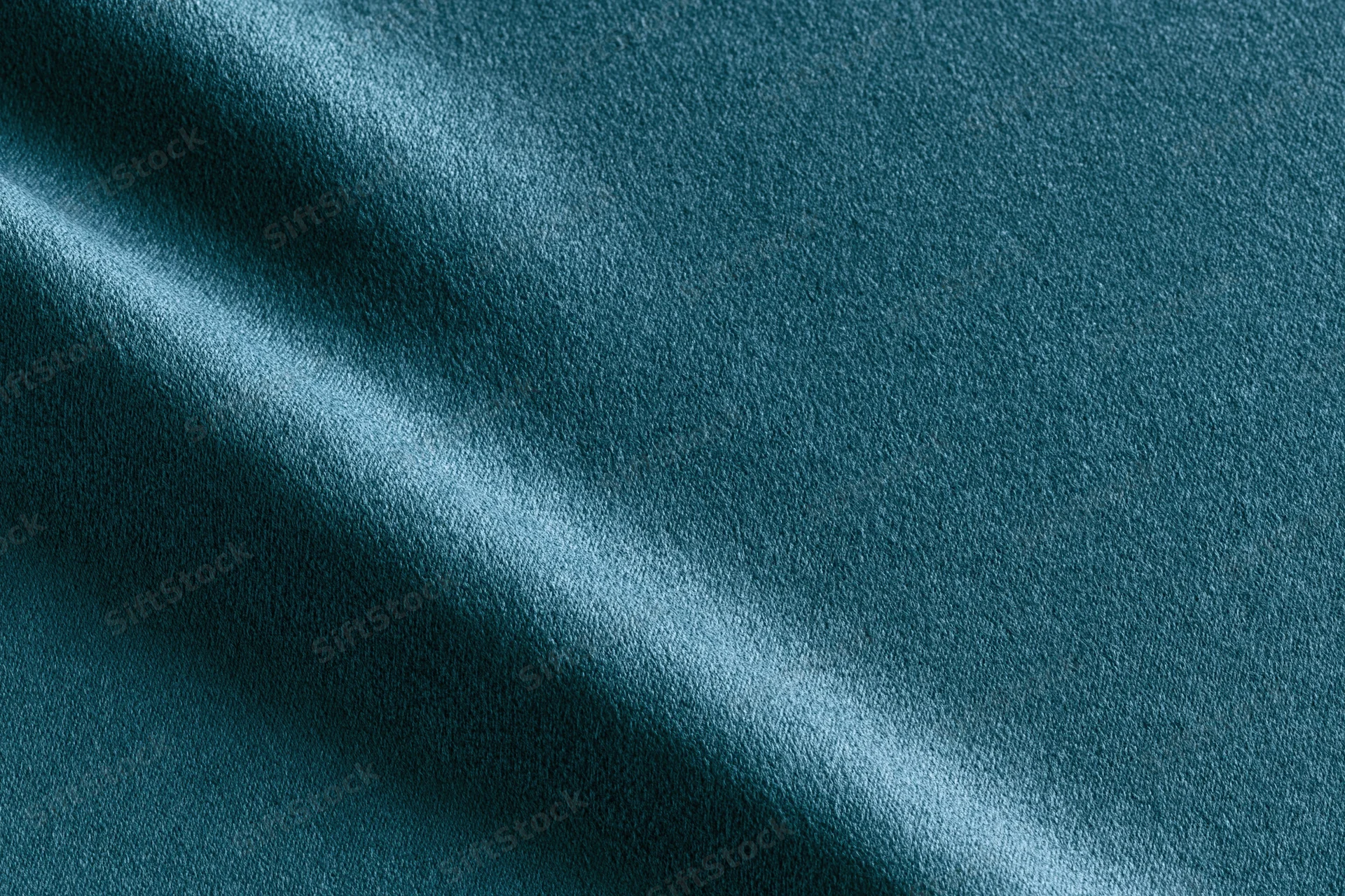Close-up flat lay of deep teal fabric filling the frame with folds and light reflections