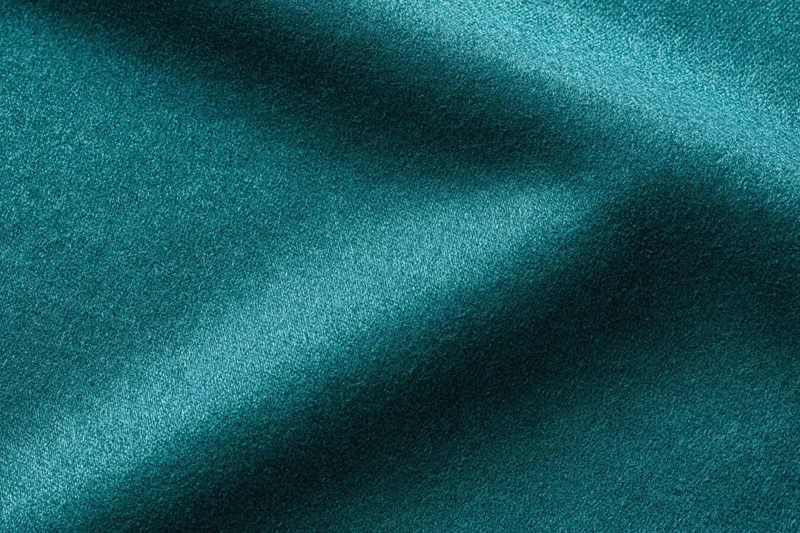 Deep teal fabric with soft folds and lustrous texture filling the frame in a flat lay closeup