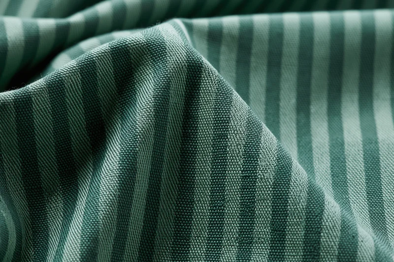 Close-up of green striped fabric textile with visible weave pattern filling the frame in a flat lay arrangement
