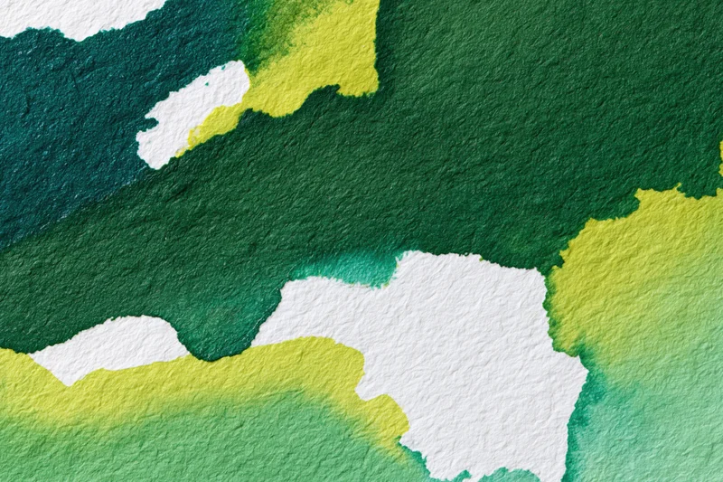 Close-up of hand-painted watercolor paper surface with green and yellow paint blending on textured white paper