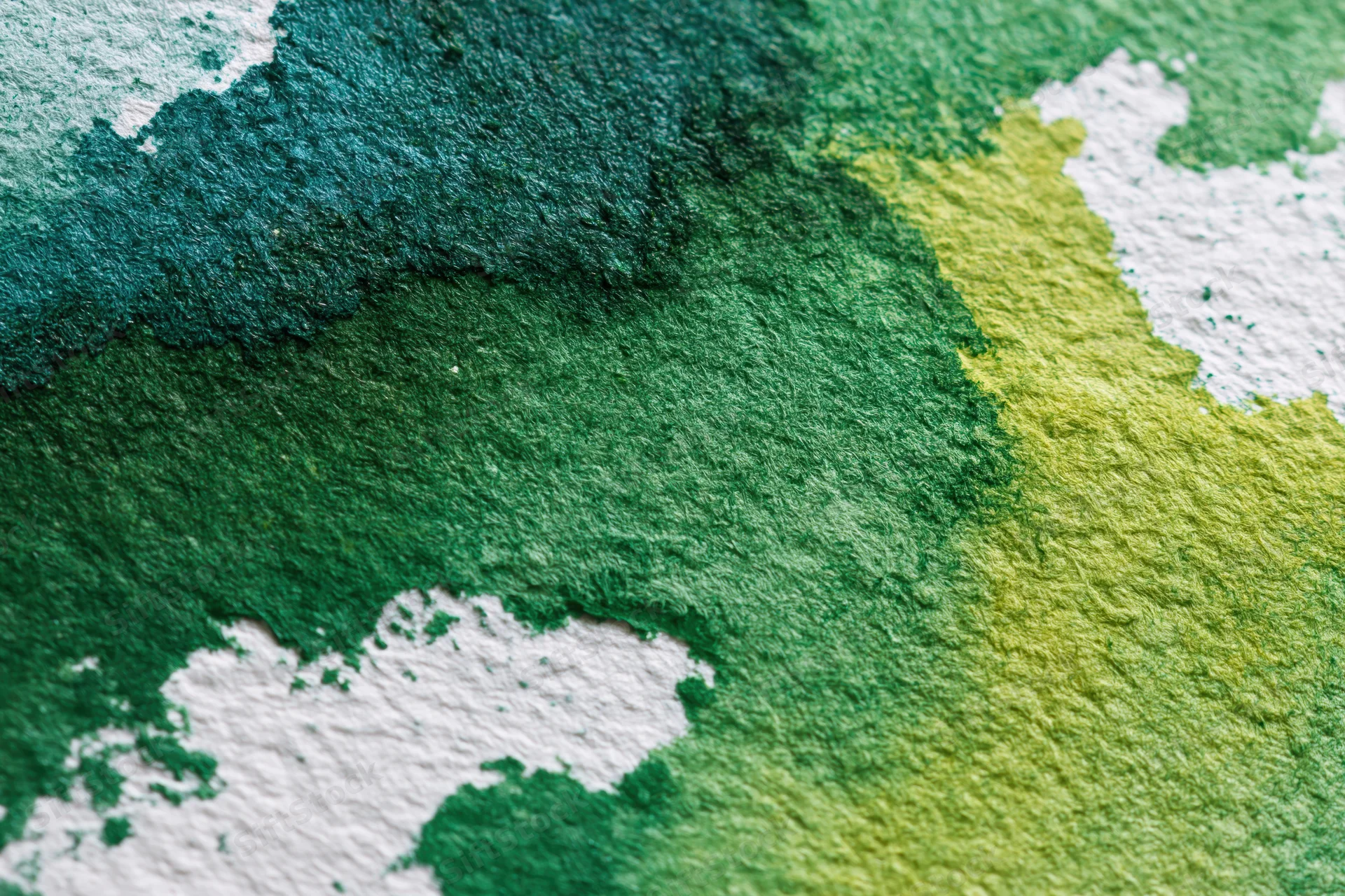 Close-up of hand-painted watercolor paper surface with green and yellow paint blends and white texture showing through