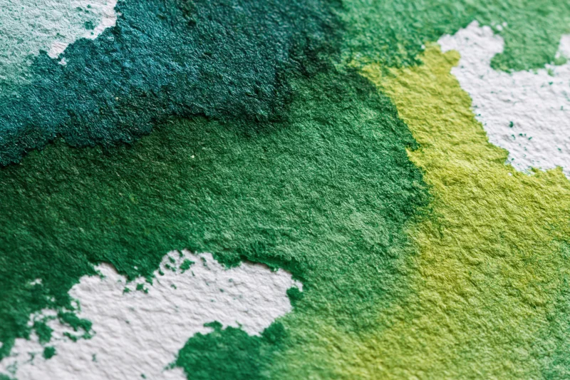 Close-up of hand-painted watercolor paper surface with green and yellow paint blends and white texture showing through