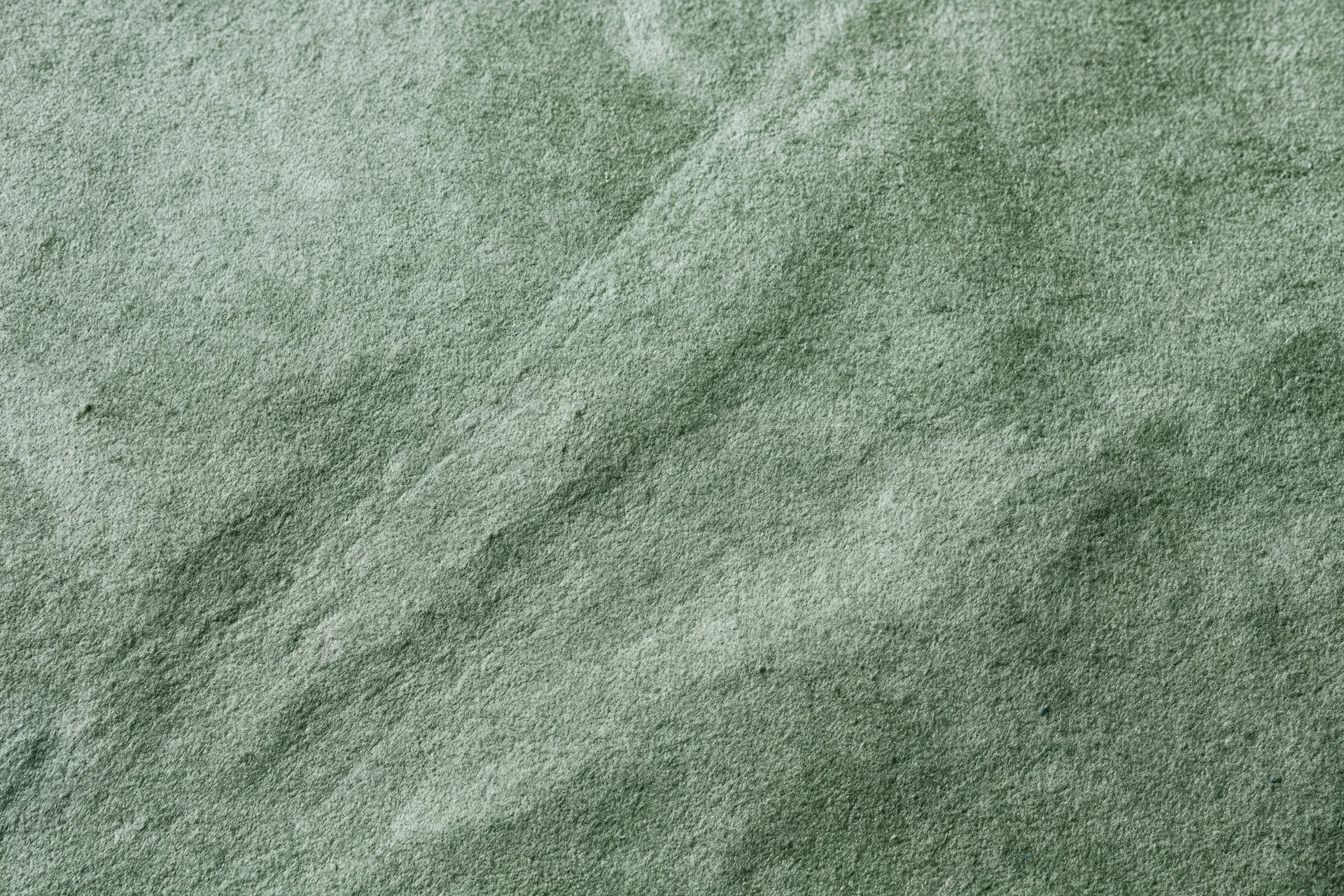 Close-up flat lay of sage green suede or velvet fabric filling the frame