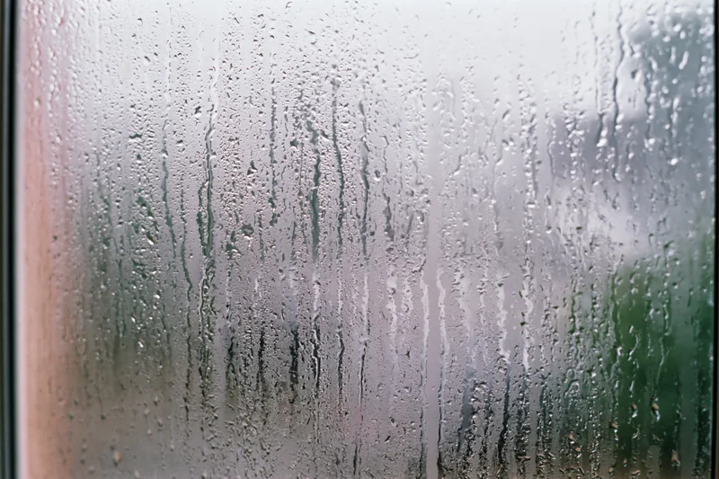 Fogged window glass covered in rain droplets and streaks with blurred outdoor view