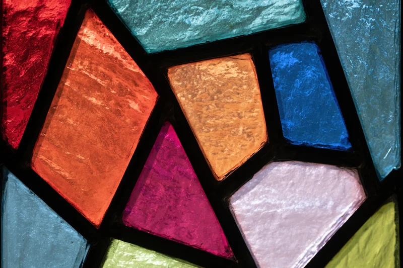 Close-up of a colorful stained glass window with geometric shapes and textured glass panels arranged in a mosaic pattern